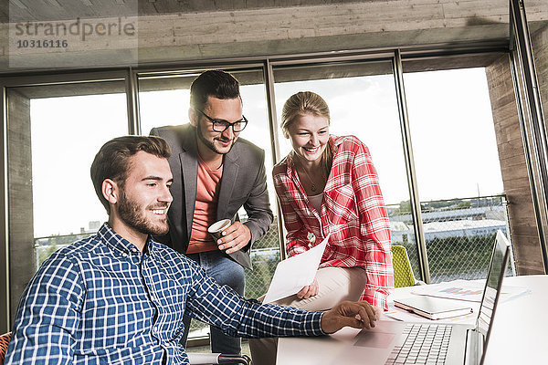 Drei lächelnde junge Leute im Konferenzraum mit Blick auf den Laptop