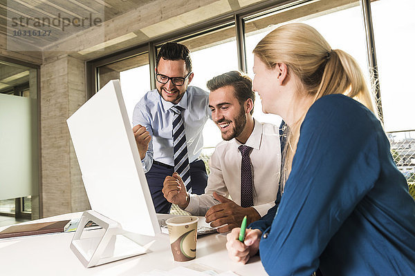 Drei glückliche junge Geschäftsleute im Konferenzraum mit Blick auf den Monitor