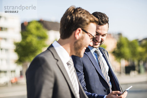 Zwei junge Geschäftsleute  die in der Stadt spazieren gehen und auf das Handy schauen.