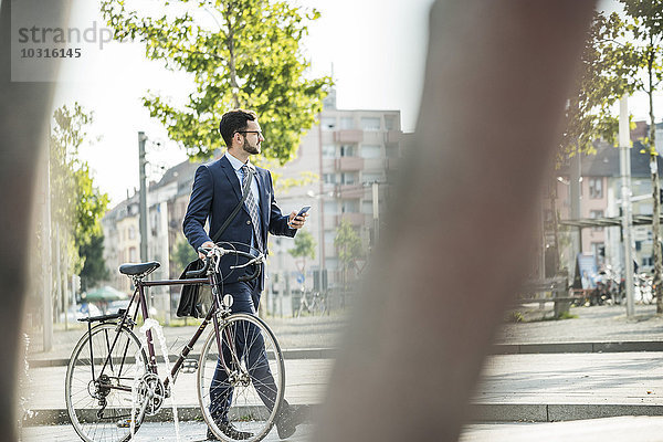 Junger Geschäftsmann schiebt Fahrrad  hält Smartphone