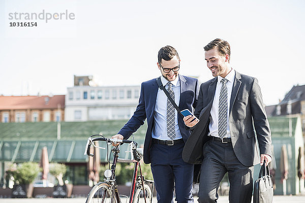 Zwei junge Geschäftsleute  die in der Stadt spazieren gehen und Fahrrad fahren.