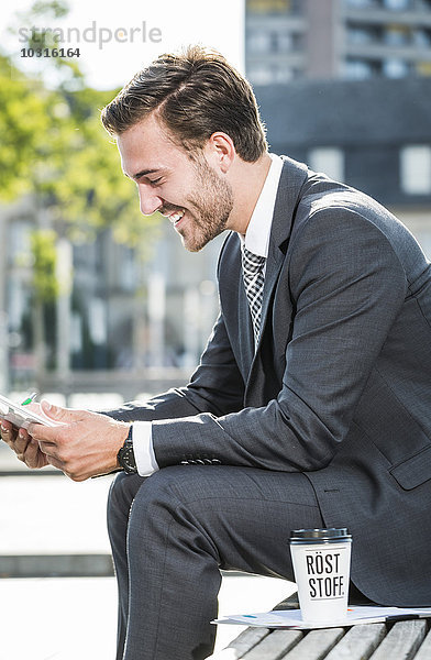 Ein junger Geschäftsmann sitzt auf einer Bank und benutzt ein digitales Tablett.