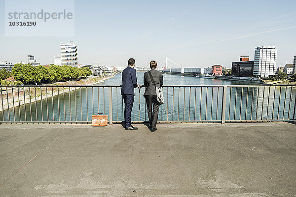 Junge Geschäftsleute stehen am Geländer und schauen auf den Fluss.