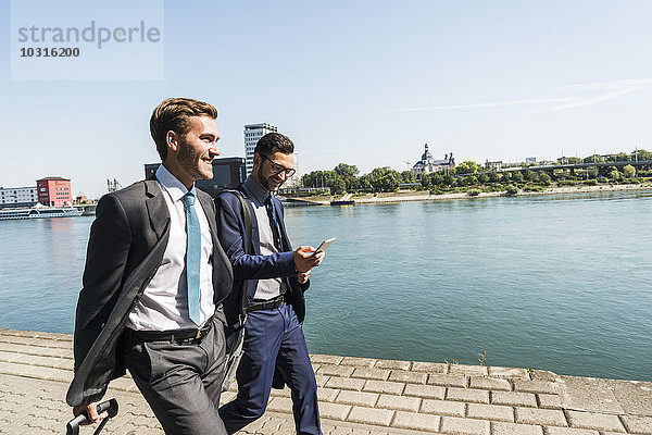 Zwei junge Geschäftsleute auf Geschäftsreise  die am Fluss spazieren gehen