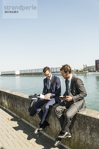 Zwei junge Geschäftsleute  die an der Wand am Fluss sitzen und arbeiten.