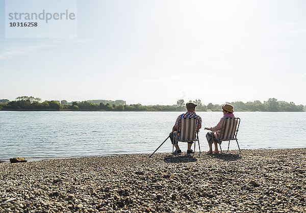 Deutschland  Ludwigshafen  Rückansicht des Seniorenpaares auf Klappstühlen am Ufer des Flusses