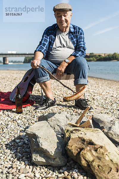 Deutschland  Ludwigshafen  Porträt eines lächelnden Senioren beim Grillen am Strand