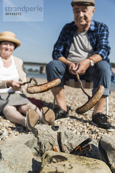 Deutschland  Ludwigshafen  Seniorenpaar Grillwürste am Strand