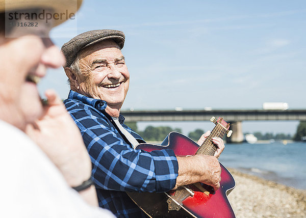 Deutschland  Ludwigshafen  Porträt des lachenden Senioren mit Gitarre am Flussufer