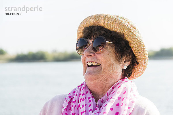 Porträt einer lächelnden Seniorin mit Sonnenbrille und Sommerhut