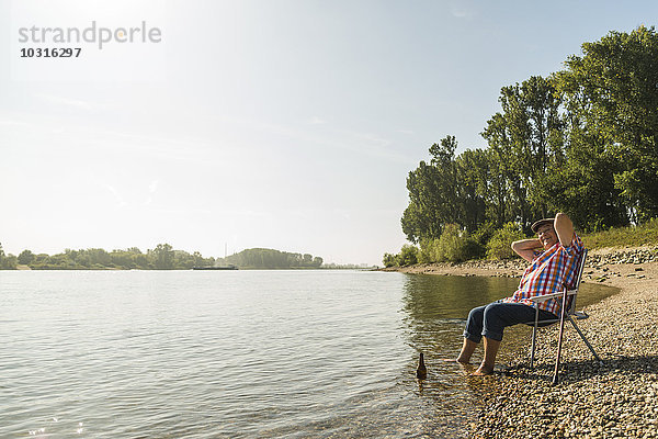 Deutschland  Ludwigshafen  fröhlicher Senior entspannt auf Klappstuhl am Flussufer