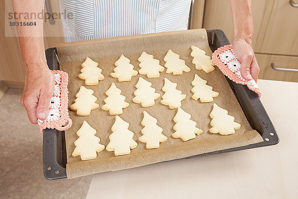 Frau hält Backblech mit Christbaumgebäck