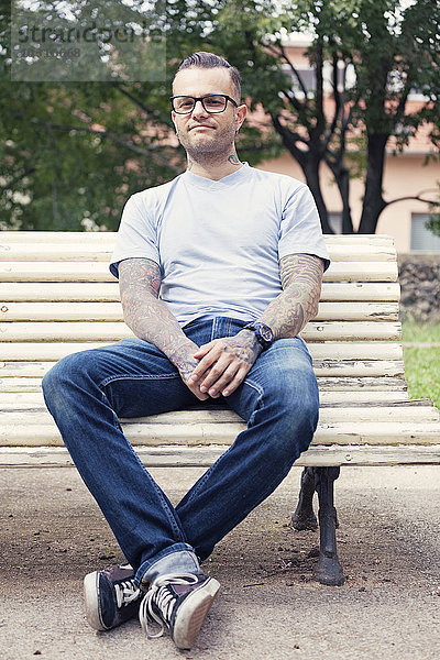 Tätowierter Mann auf einer Parkbank sitzend