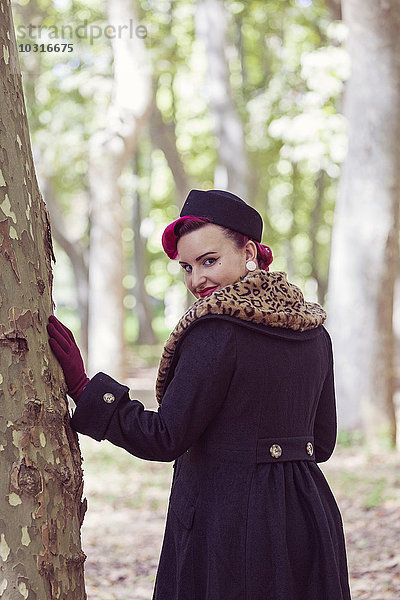 Porträt einer modischen jungen Frau mit farbigen Haaren  die über die Schulter im Wald blickt.