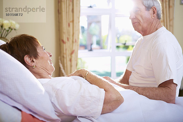 Seniorenfrau im Krankenhausbett im Gespräch mit Seniorenmann