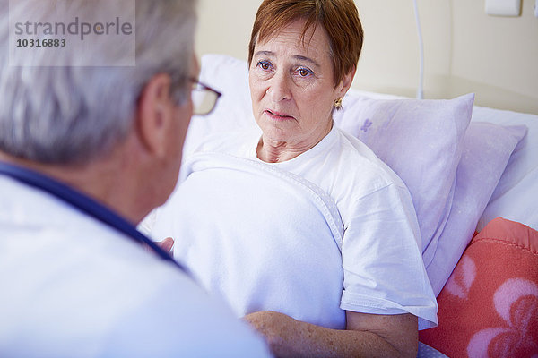 Arzt im Gespräch mit Seniorin im Krankenhausbett liegend