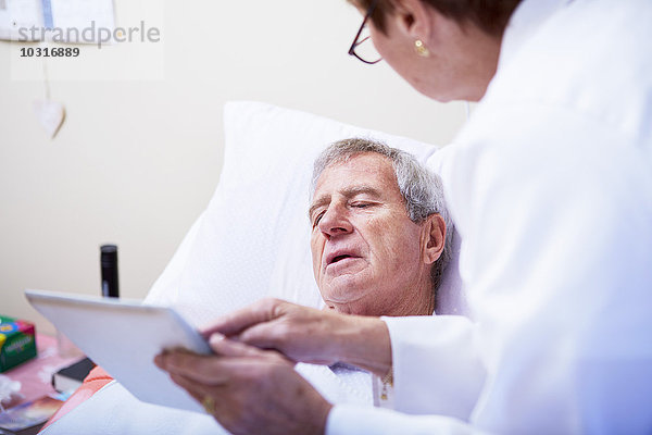 Arzt zeigt digitales Tablett für Senioren im Krankenhausbett