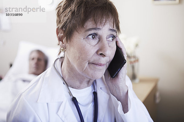 Seriöser Arzt am Telefon mit Patient im Krankenhausbett