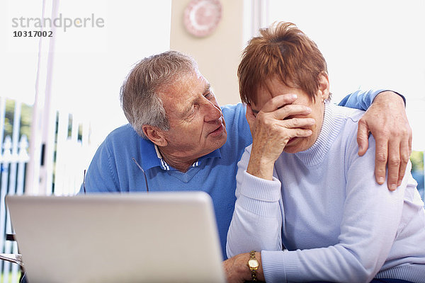Senior Mann tröstet weinende Frau am Laptop