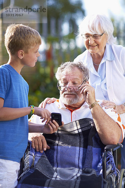 Großmutter und Enkel erklären Großvater im Rollstuhl Handy