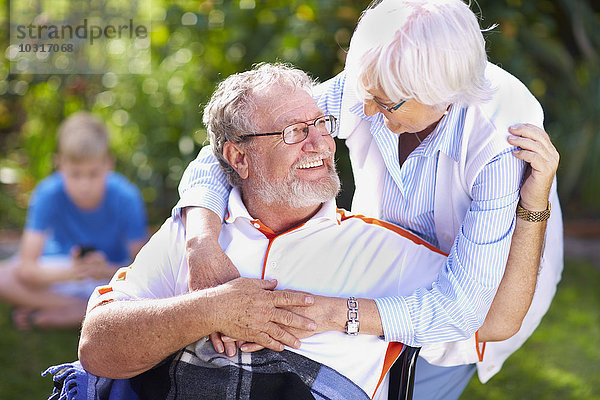Seniorin umarmt Ehemann im Rollstuhl