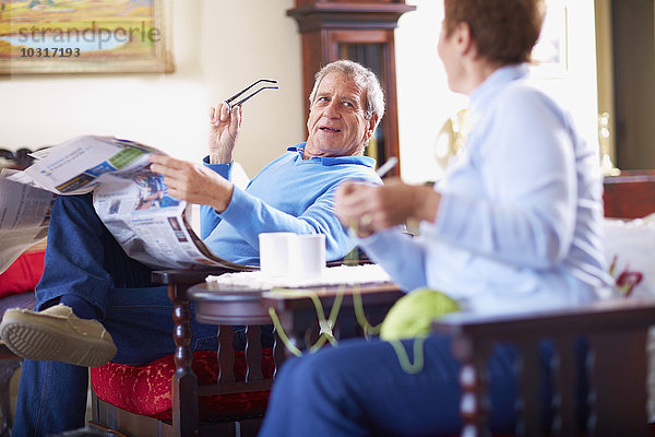 Älterer Mann mit Zeitung zu Hause im Gespräch mit Frau