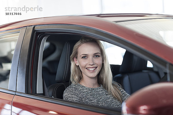 Lächelnde junge Frau im neuen Auto sitzend