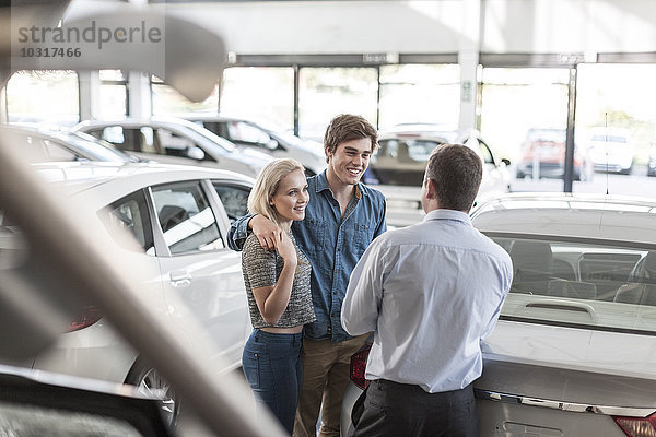 Autohändler im Gespräch mit einem jungen Paar im Showroom