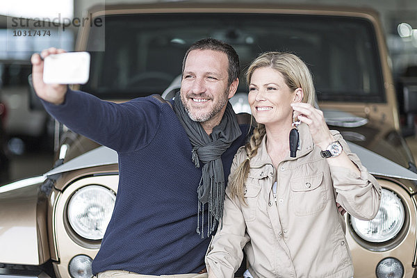 Glückliches Paar im Autohaus nimmt Selfie vor dem neuen Auto