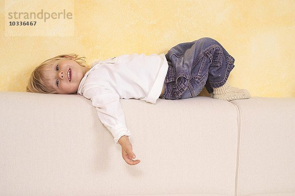 Kind liegt auf einem Sofa und lacht