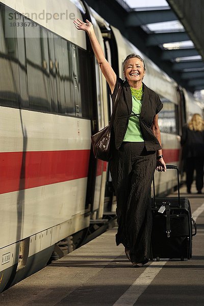 Ältere Frau mit Trolley winkt auf dem Bahnsteig
