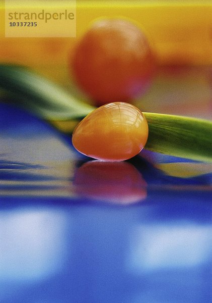 orange Glaskugel liegt mit grünem Blatt auf Wasser