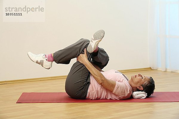 Ältere Frau macht Bodenübungen auf einer Matte - Seniorin dehnt ihre Muskeln im Gesäß - weniger Schmerzen