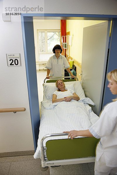 Patientin wird von Krankenschwestern in ihrem Bett über einen Krankenhausboden bewegt