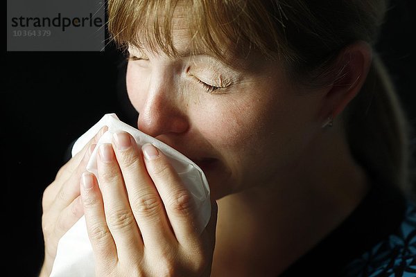 Junge erwachsene Frau hat Schnupfen  muss niesen  putzt sich die Nase mit einem Taschentuch