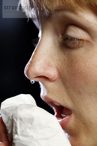 Junge erwachsene Frau hat Schnupfen  muss niesen  putzt sich die Nase mit einem Taschentuch. Die Nase tropft