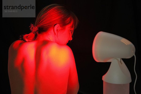 Junge erwachsene Frau lässt sich gegen Erkältungen  Verstauchungen  Schmerzen  von einer ultravioletten heißen Lite-Lampe anstrahlen