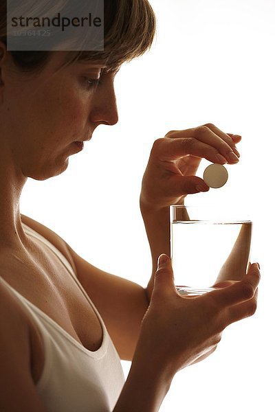 Junge erwachsene Frau löst eine Brausetablette in einem Glas mit Wasser auf