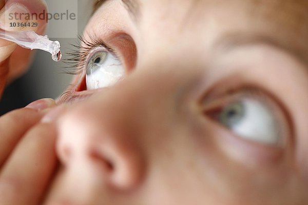 Junge erwachsene Frau tropft sich Augentropfen ins Auge