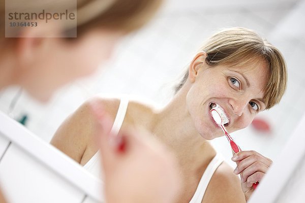 Junge erwachsene Frau putzt sich die Zähne in einem Badezimmer