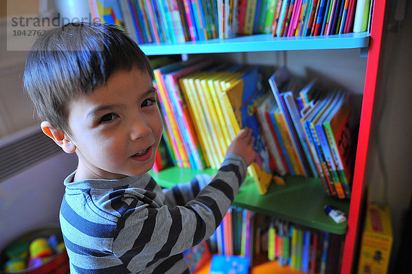 4 Jahre alter Junge sucht sich ein Buch aus seiner Bibliothek aus