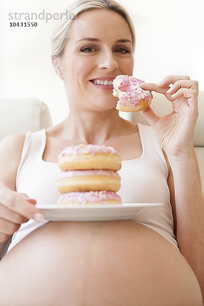 MODELL FREIGEGEBEN. Schwangere Frau isst einen Teller mit Donuts. Sie ist im 8. Monat schwanger.