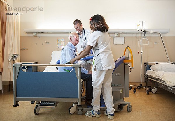 MODELL FREIGEGEBEN. Pflegekräfte helfen einem Patienten mit einem aktiven Lifter aus dem Bett Pflegekräfte helfen einem Patienten aus dem Bett