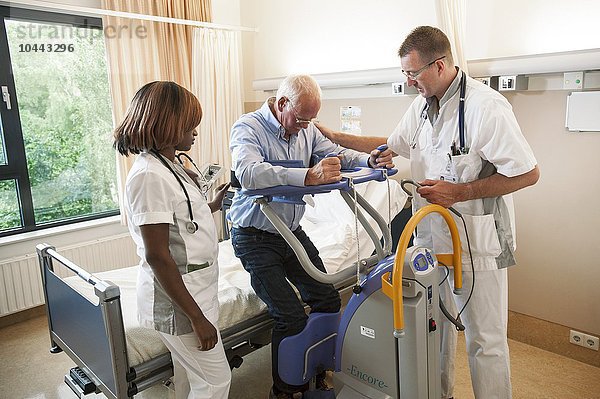 MODELL FREIGEGEBEN. Pflegekräfte helfen einem Patienten mit einem aktiven Lifter aus dem Bett Pflegekräfte helfen einem Patienten aus dem Bett