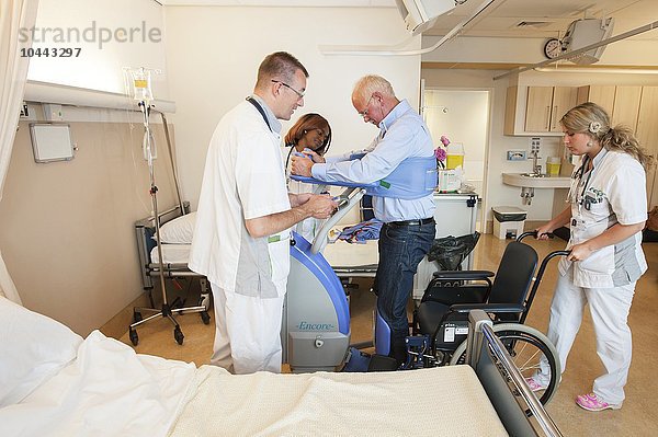MODELL FREIGEGEBEN. Pflegekräfte helfen einem Patienten mit einem aktiven Lifter aus dem Bett und in einen Rollstuhl Pflegekräfte helfen einem Patienten aus dem Bett