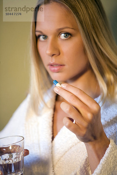 Frau hält eine Pille und ein Glas Wasser