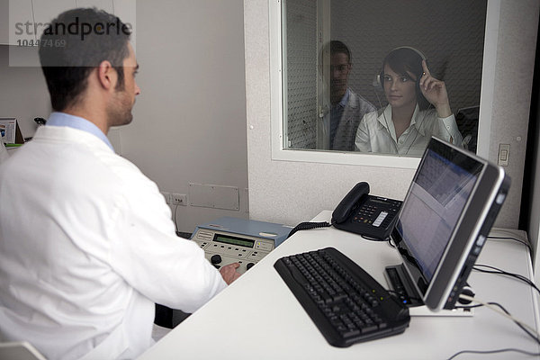 männlicher Arzt und weibliche Patientin in audiometrischen Untersuchungskabinen  audiometrischer Test