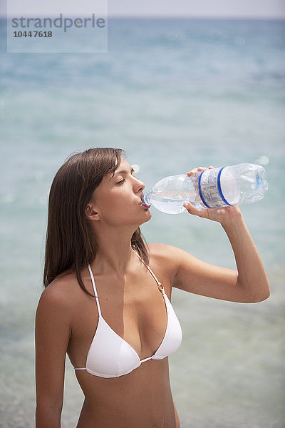 junge Frau mit einer Flasche Wasser am Meer stehend