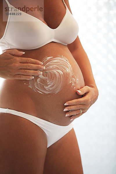 Schwangere Frau trägt Feuchtigkeitscreme auf den Bauch auf