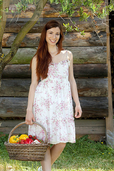 eine lächelnde Frau mit einem Korb voller Gemüse in einem Garten